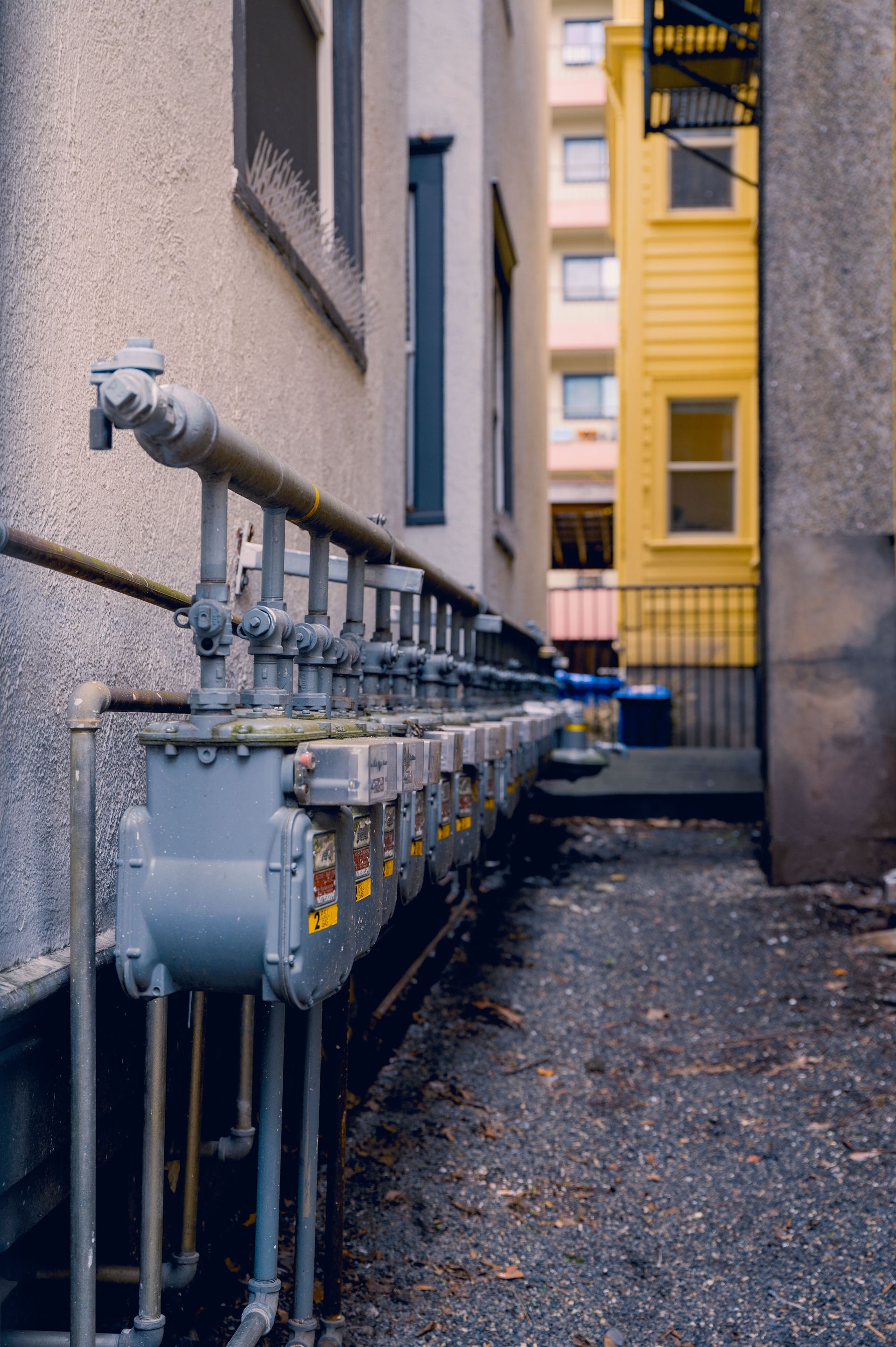 Row of gas meters with pipes in a narrow urban alleyway, captured in a vertical shot.